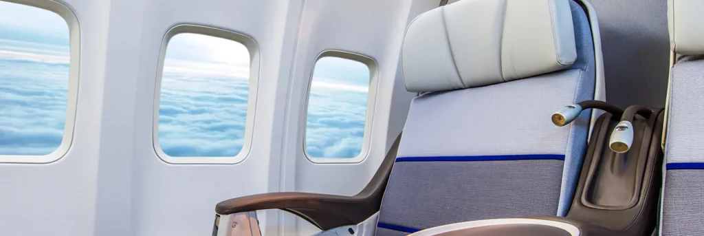 Vue intérieure d'une cabine d'avion avec des sièges confortables et de grandes fenêtres, offrant une vue sur les nuages en contrebas. L'image suggère un environnement de voyage d'affaires agréable et professionnel.