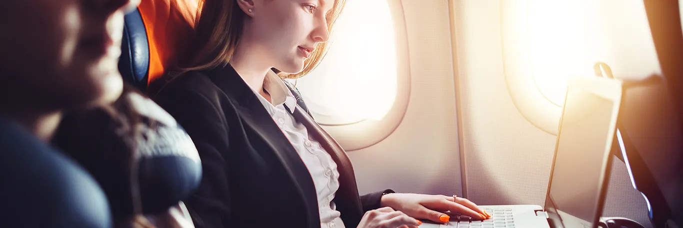 Femme d'affaires travaillant sur un ordinateur portable à bord d'un avion, éclairée par la lumière du hublot. L'image illustre la productivité et la connectivité en déplacement, soulignant les services de CTA Business Travel pour permettre aux voyageurs d'affaires de rester efficaces pendant leurs trajets.