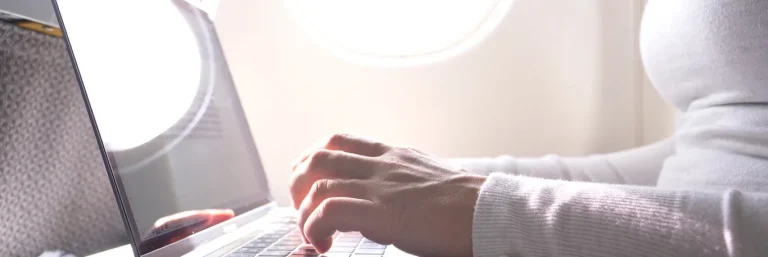 Personne travaillant sur un ordinateur portable à bord d'un avion, avec la lumière du jour entrant par le hublot. L'image illustre la productivité et la connectivité en déplacement, soulignant les services de CTA Business Travel pour permettre aux collaborateurs de rester efficaces pendant les voyages d'affaires.