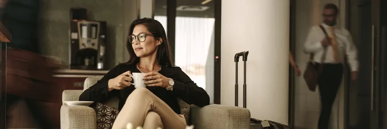 Femme d'affaires assise dans un salon d'aéroport, tenant une tasse de café, avec une valise à ses côtés. L'image représente la détente et le confort lors des déplacements professionnels, mettant en avant les services de CTA Business Travel pour assurer une gestion sans stress des voyages d'affaires.