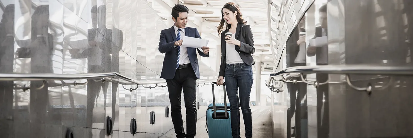 Deux professionnels, un homme et une femme, marchant dans un aéroport avec des documents et une valise à roulettes, tout en discutant. L'image illustre la collaboration et la préparation lors des déplacements professionnels, soulignant les services de CTA Business Travel pour organiser et faciliter les voyages d'affaires.