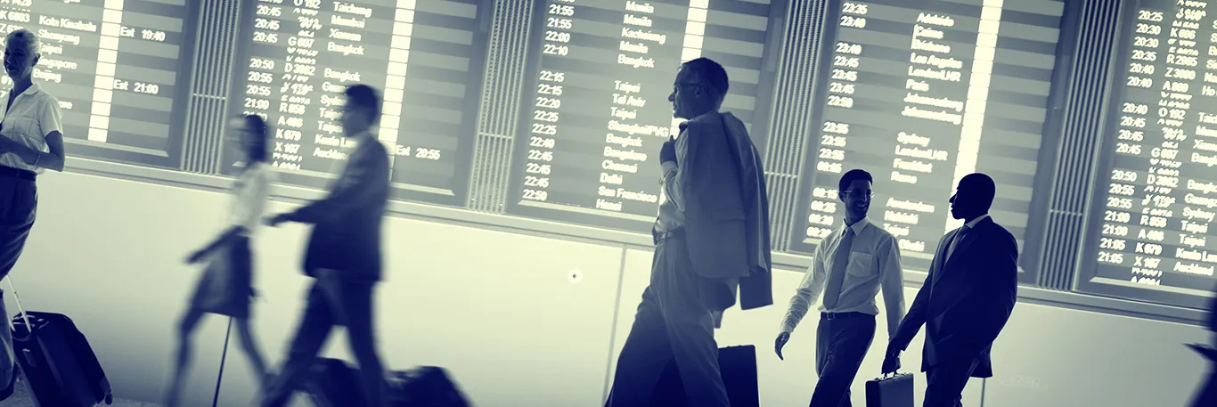 Voyageurs d'affaires marchant devant un tableau d'affichage des vols dans un aéroport. L'image représente l'activité et la mobilité des professionnels en déplacement, soulignant les services de CTA Business Travel pour organiser et gérer efficacement les voyages d'affaires.