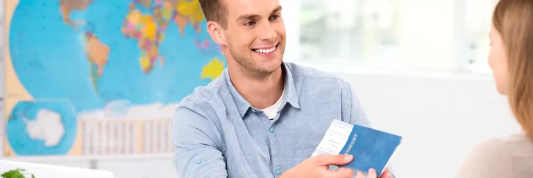 Jeune homme souriant remettant un passeport et des billets d'avion à une personne dans un bureau de voyage, avec une carte du monde en arrière-plan. L'image illustre les services personnalisés et l'assistance fournie par CTA Business Travel pour organiser et gérer les voyages d'affaires.