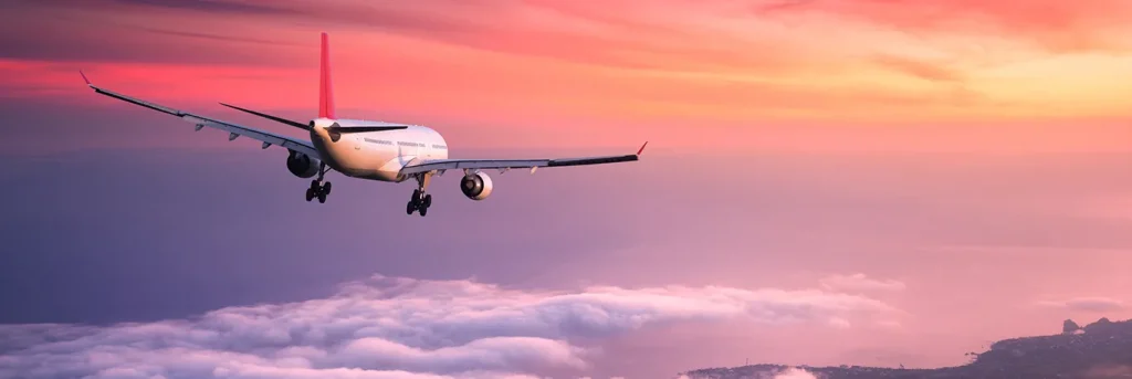 Avion volant au-dessus des nuages à l'aube, avec un ciel aux teintes rosées. L'image représente les voyages d'affaires internationaux, mettant en avant l'engagement de CTA Business Travel à offrir des services de gestion de déplacements professionnels efficaces et agréables.