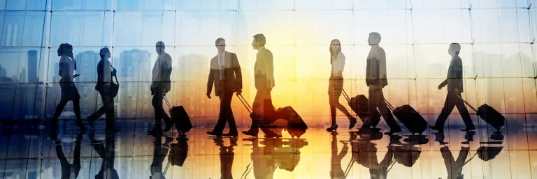 Silhouettes de professionnels tirant des valises à roulettes, marchant dans un aéroport au lever du soleil. L'image évoque le dynamisme et la fréquence des déplacements professionnels, soulignant l'engagement de CTA Business Travel à faciliter les voyages d'affaires pour les collaborateurs.