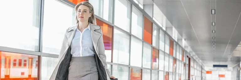 Femme d'affaires marchant dans un couloir d'aéroport avec une valise à roulettes. L'image représente la mobilité et le professionnalisme des déplacements professionnels, illustrant les services de CTA Business Travel pour accompagner les entreprises dans leurs voyages d'affaires.