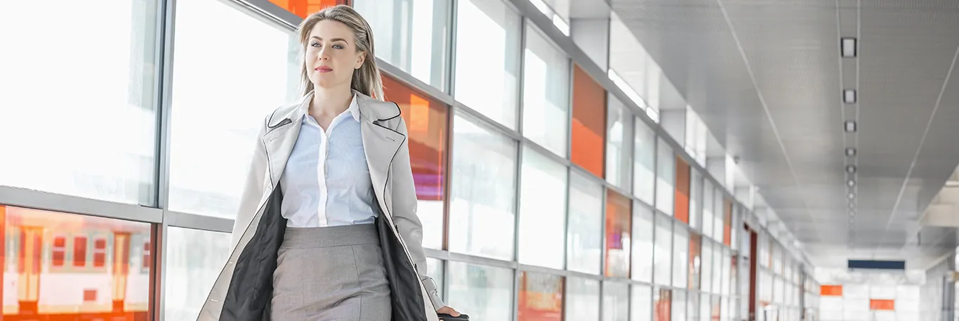 Femme d'affaires marchant dans un couloir d'aéroport avec une valise à roulettes. L'image représente la mobilité et le professionnalisme des déplacements professionnels, illustrant les services de CTA Business Travel pour accompagner les entreprises dans leurs voyages d'affaires.