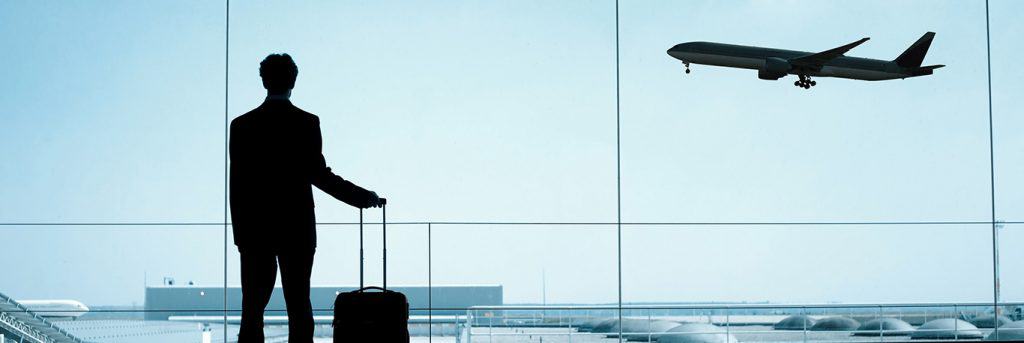 Silhouette d'un homme d'affaires avec une valise, regardant un avion décoller depuis une grande fenêtre d'aéroport. L'image illustre les voyages d'affaires internationaux, mettant en avant la mobilité et la connectivité des professionnels, ainsi que les services de CTA Business Travel pour faciliter ces déplacements.