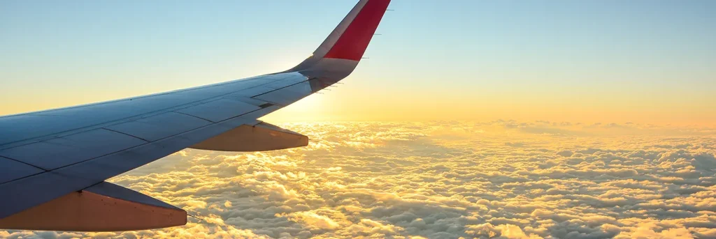 Aile d'un avion en vol au-dessus d'une mer de nuages au coucher du soleil. L'image évoque la tranquillité et l'efficacité des voyages d'affaires, soulignant l'engagement de CTA Business Travel à offrir une expérience de voyage professionnelle fluide et agréable.