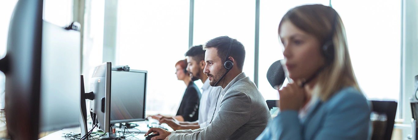 Des agents de support client en tenue professionnelle travaillant dans un centre d'appels, portant des casques avec micro et concentrés sur leurs écrans d'ordinateur. Cette image illustre le service de conciergerie de voyage d'affaires offert par CTA Business Travel, mettant en avant la disponibilité, le professionnalisme et la réactivité de l'équipe pour assister les clients en tout temps.