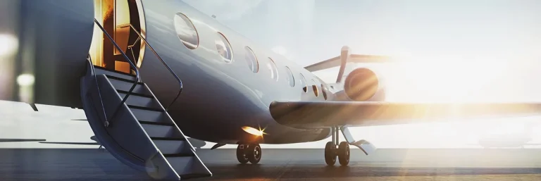 Un jet privé stationné sur le tarmac, avec la porte ouverte et les escaliers déployés, illuminé par le soleil levant ou couchant. Cette image illustre les services VIP de voyage d'affaires offerts par CTA Business Travel, mettant en avant le luxe, la commodité et l'exclusivité des déplacements en jet privé.