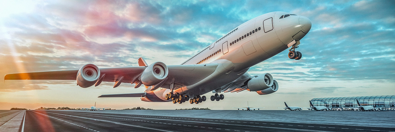 Un avion de ligne en phase de décollage sur une piste d'aéroport au coucher du soleil, avec des couleurs chaudes et un ciel partiellement nuageux. À l'arrière-plan, des avions et des structures d'aéroport sont visibles. Cette image illustre la dynamique et l'efficacité des services de voyage d'affaires offerts par CTA Business Travel, mettant en avant la ponctualité et la connectivité internationale.