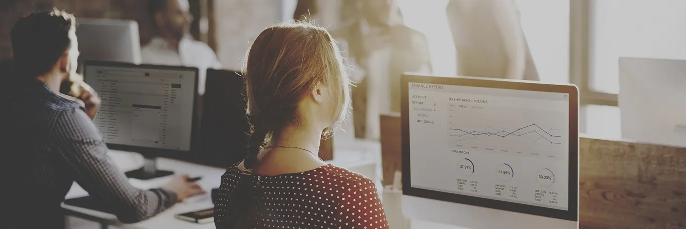 Des employés Des employés travaillent dans un bureau moderne et lumineux. Au premier plan, une femme regarde un écran d'ordinateur affichant un tableau de bord financier avec des graphiques et des statistiques. D'autres collègues, concentrés sur leurs propres écrans, sont visibles en arrière-plan. La lumière naturelle du soleil illumine l'espace de travail, créant une ambiance productive et professionnelle. Cette image illustre l'importance de l'analyse et du reporting dans la gestion efficace des voyages d'affaires.